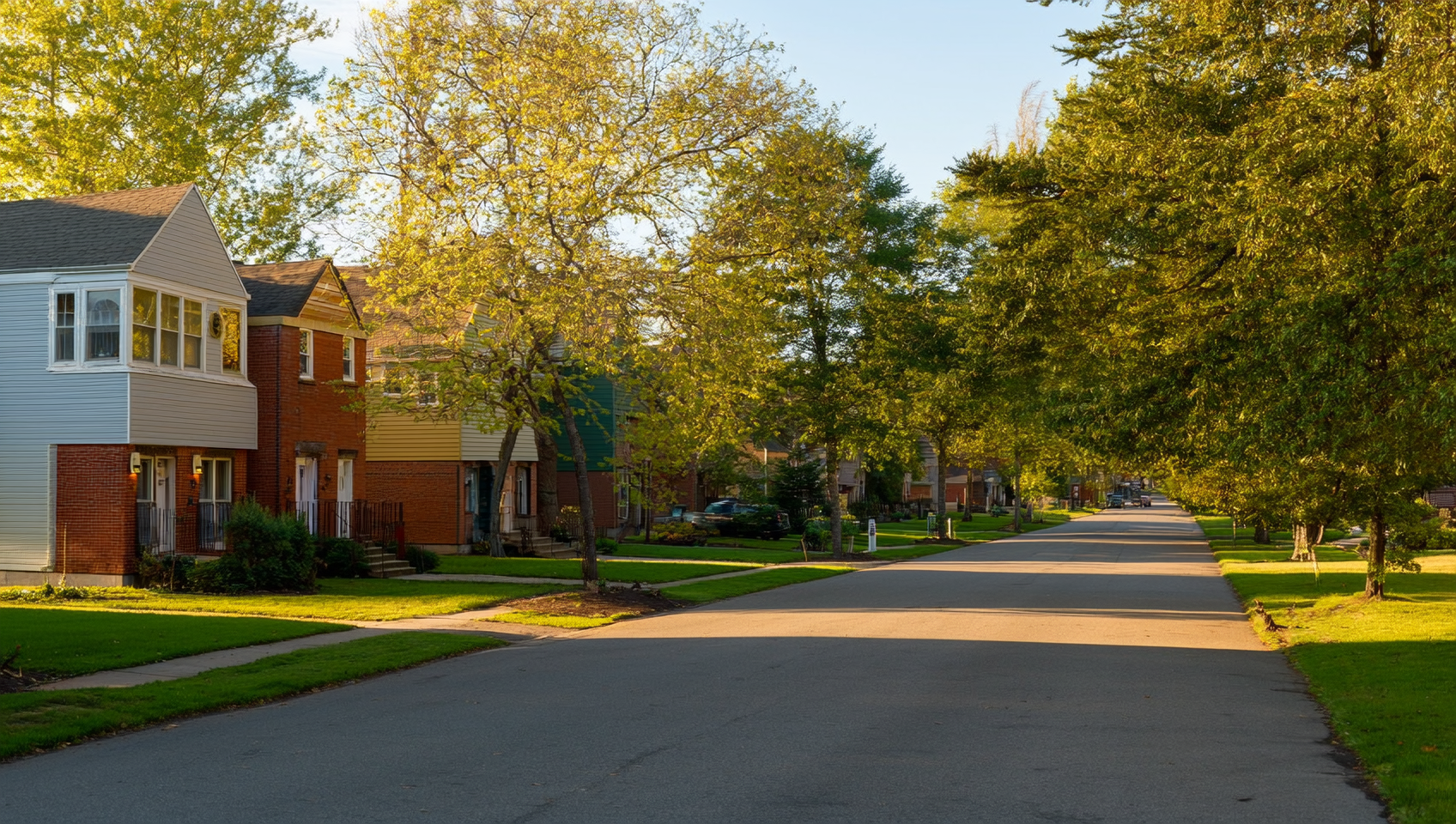 A quiet Barrie street with detached brick and siding houses, mature trees and empty driveways bathed in afternoon light