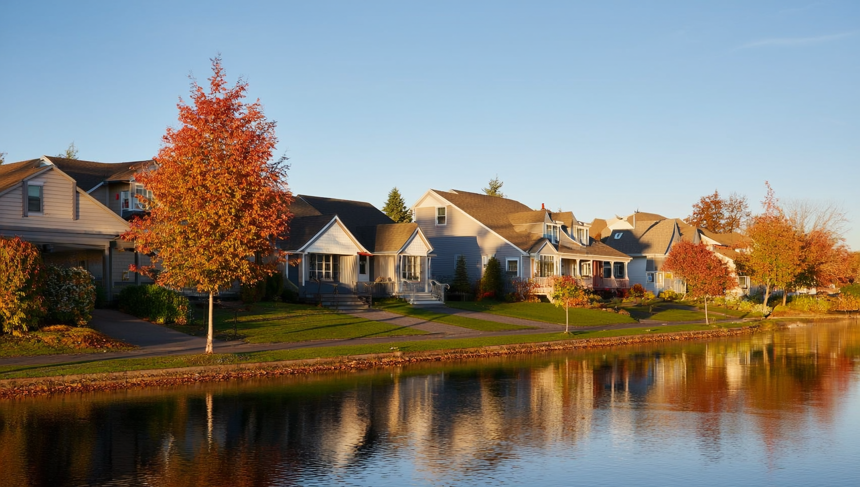 A quiet Orillia residential street with detached homes, mature trees, and autumn foliage reflected in Lake Couchiching