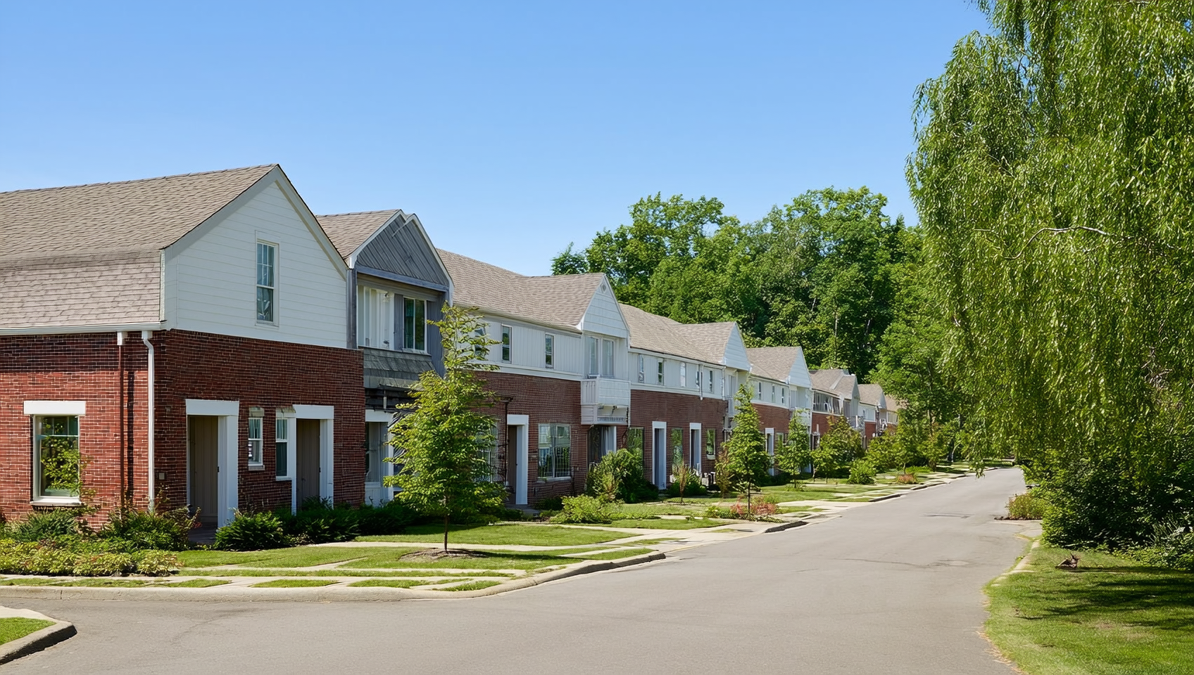 A row of modern brick-and-wood townhomes with gable roofs lines a quiet Aurora street framed by summer trees